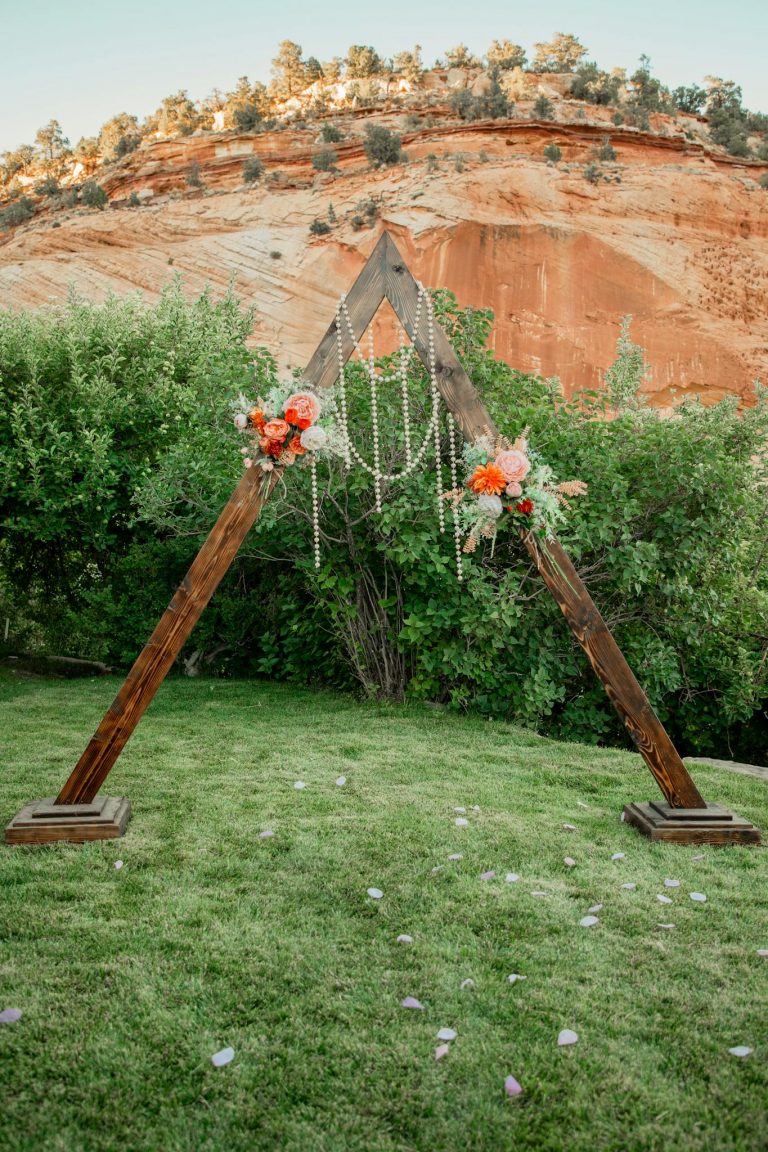 A triangle wooden arch adorned with flowers and pearls in a picturesque outdoor landscape.