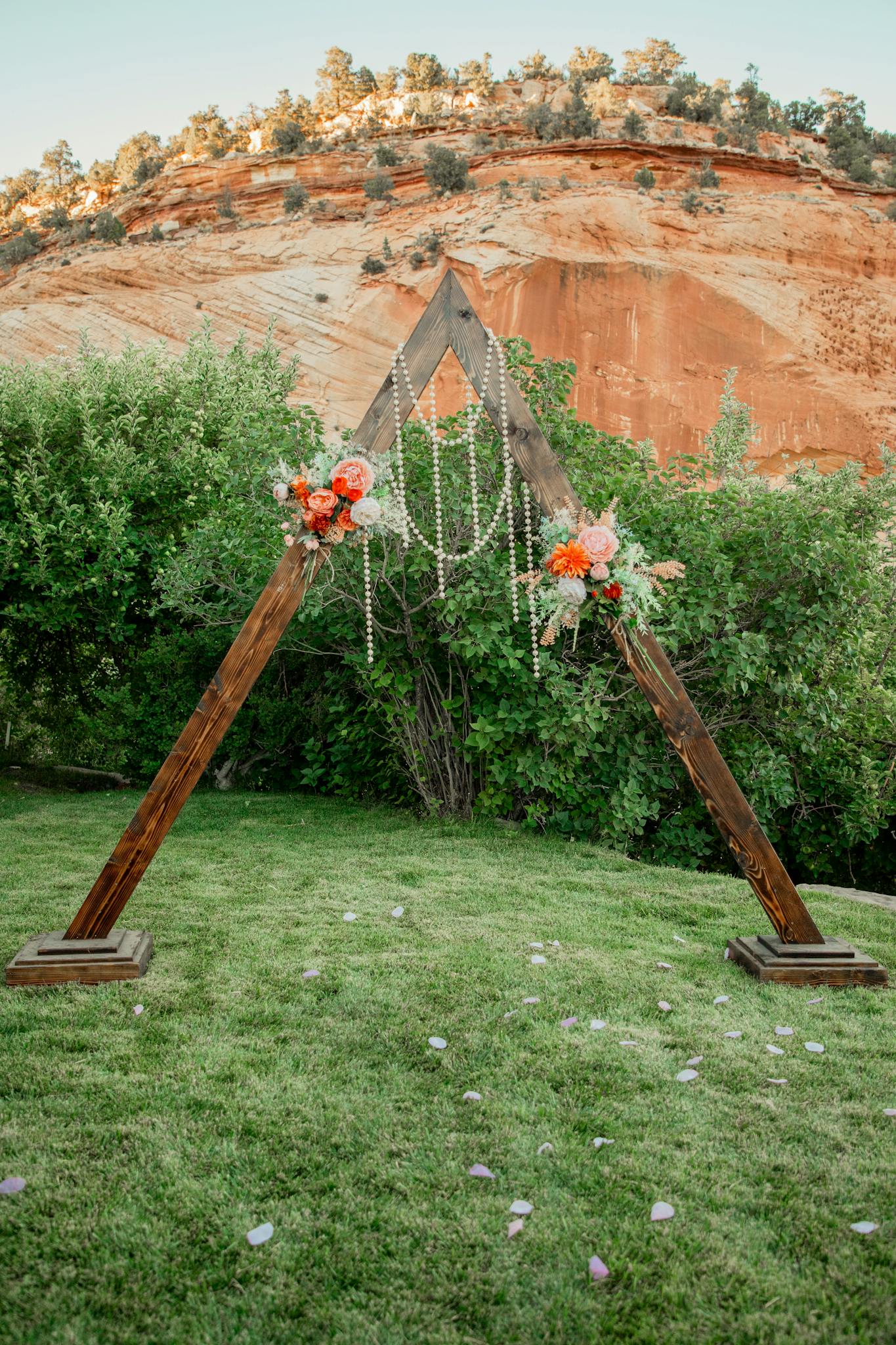 A triangle wooden arch adorned with flowers and pearls in a picturesque outdoor landscape.